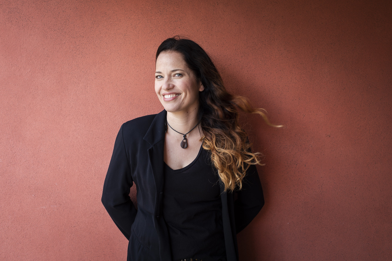 Katja Frenzel lacht herzlich vor einer terrakottafarbenen Wand