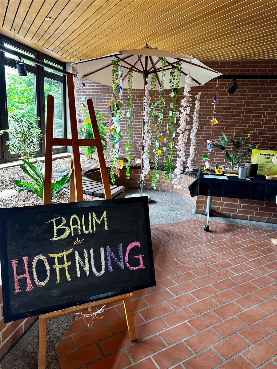 Der Baum der Hoffnung: ein Schirm voller Blütenranken und handgeschriebener Botschaften, davor eine Kreidetafel